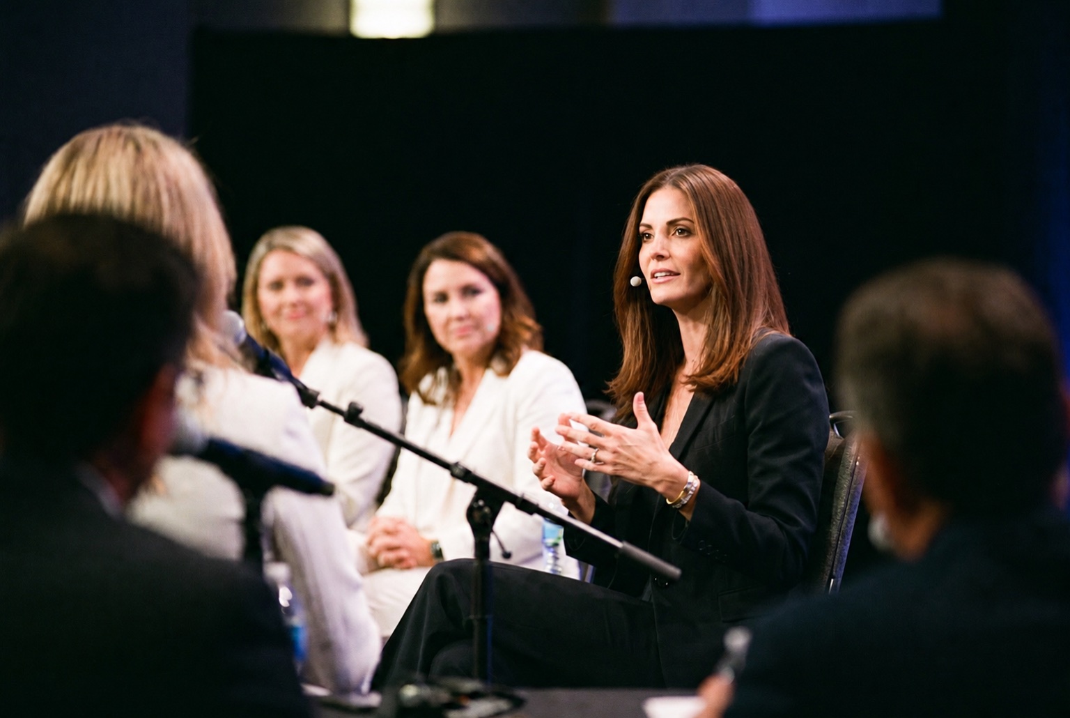 Illustrative editorial photograph of Cara Knapp answering a panel question with straighter chestnut hair